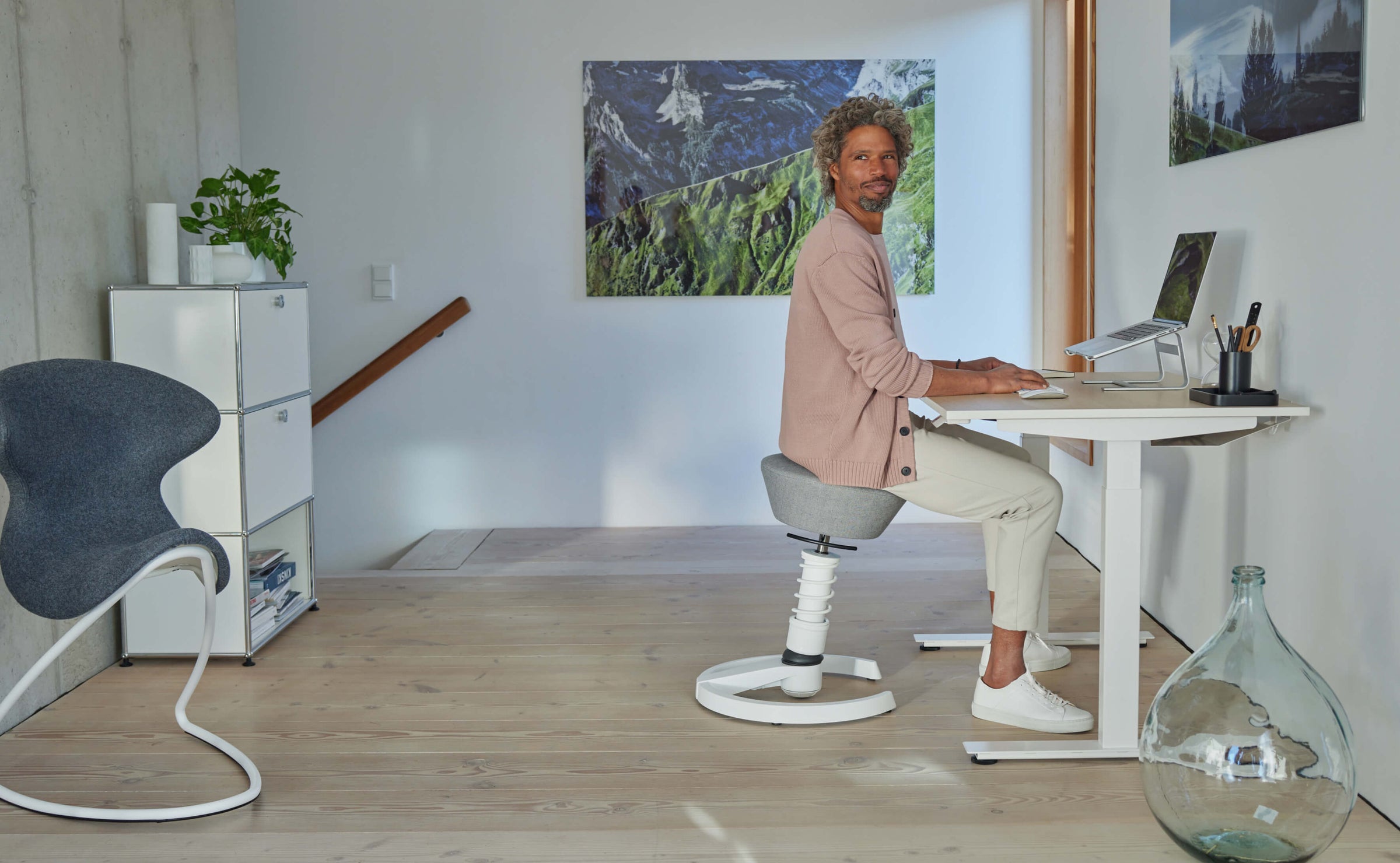 A man is working in an upright position at his desk in his study. He is sitting on the Aeris Swopper.