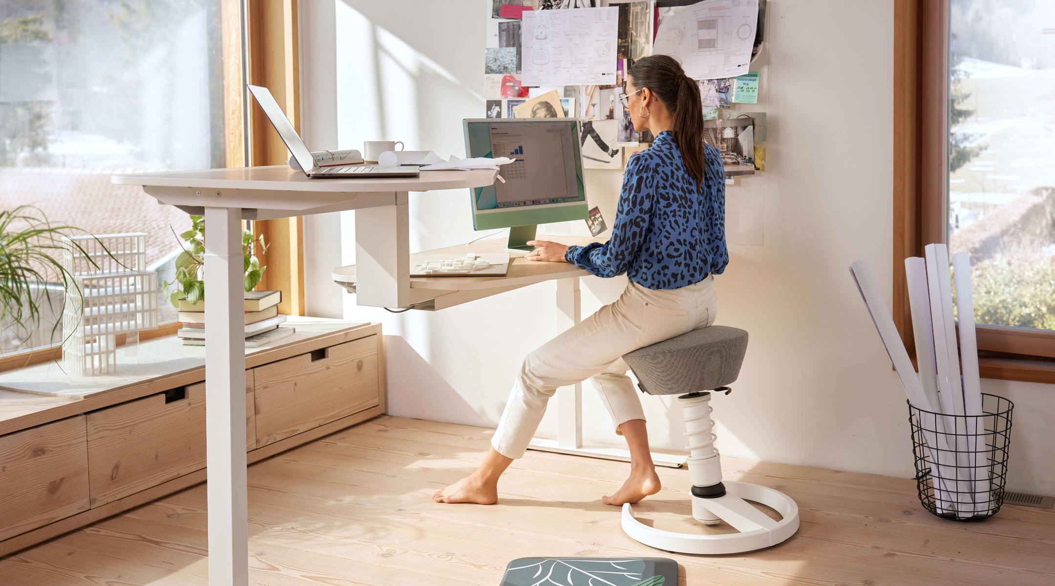 A woman is sitting on the Aeris Swopper at her double desk working on her laptop. She leans forward and the Swopper seat follows her movement.