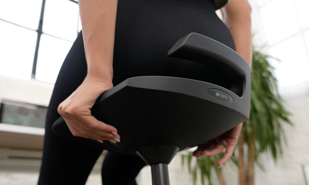 Image detail of the bottom of the Aeris Muvman seat. It shows a woman using the easy-touch buttons to adjust the height of the seat.