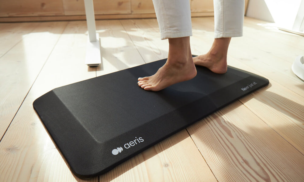 Image detail of a woman's feet standing on the anti-fatigue mat Aeris Muvmat with black cover.