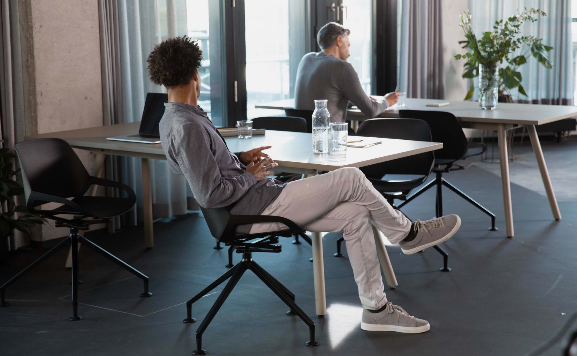 A guy leans back on the black design chair Aeris Numo. The seat shell and the backrest move with him.