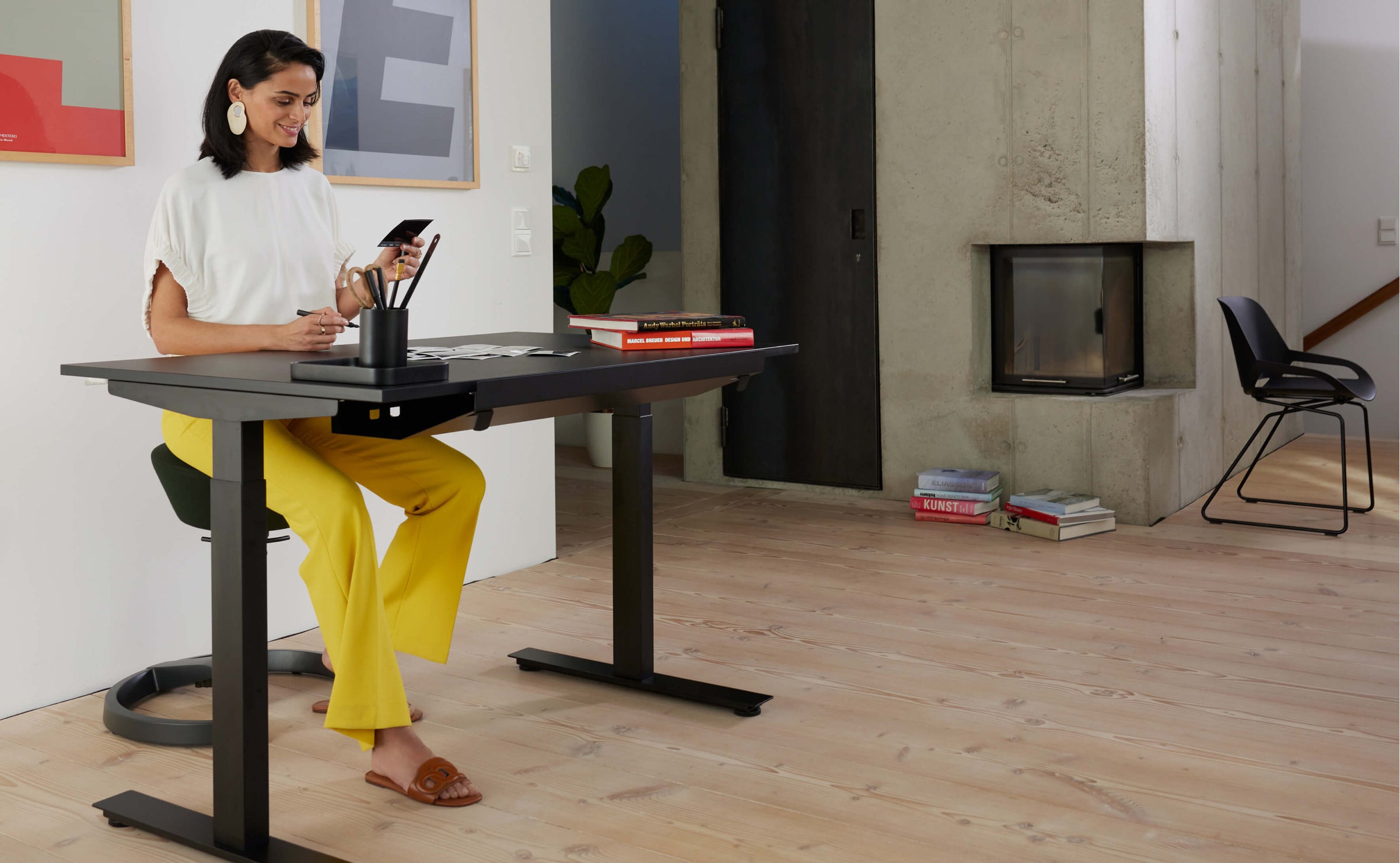 A woman is sitting on Aeris Swopper while looking at pictures at a height adjustable desk in her living-room.